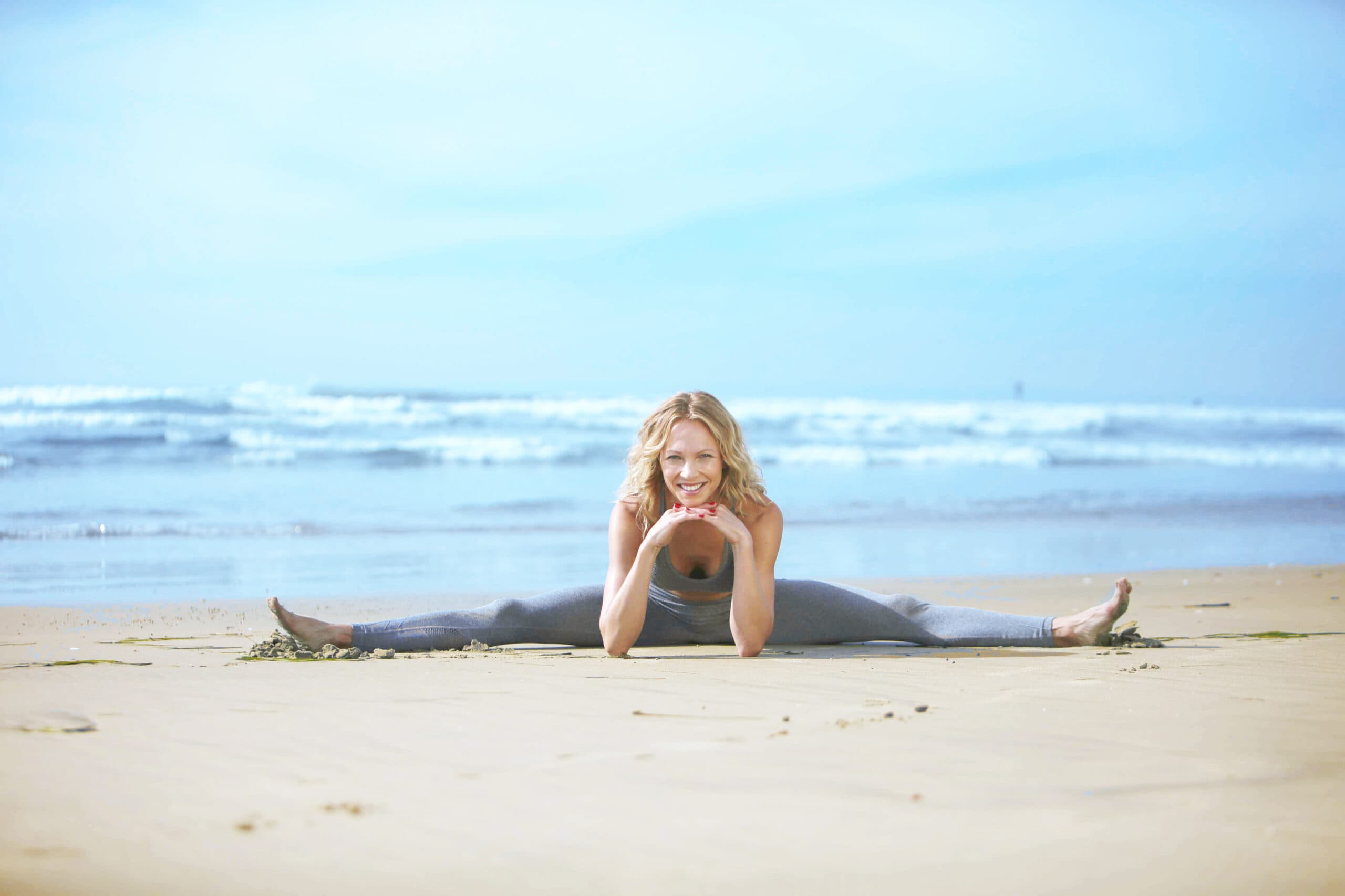 Auf dem Bild ist Birte Glang wie sie Schlank nach der Geburt im Spagat am Strand sitzt. Damit zeigt sie wie stillen und sport nach der schwangerschaft kombinierbar sind.